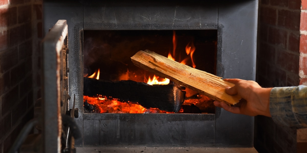 A person putting wood into a wood burning stove installed in a fireplace